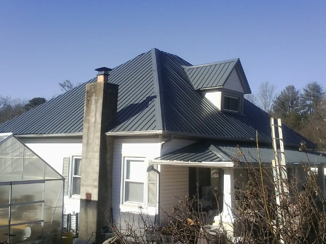 Dark blue standing seam metal roof on a white farmhouse with dormer — Slate & Tile Roof Repair by Roofing Brothers in Fair Haven