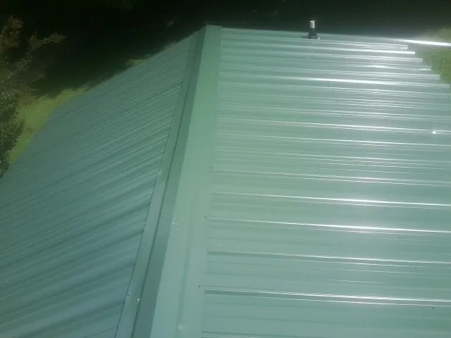 New green metal panels meeting at the ridge of a roof — Flat Roof Repair work by our crew in Fair Haven