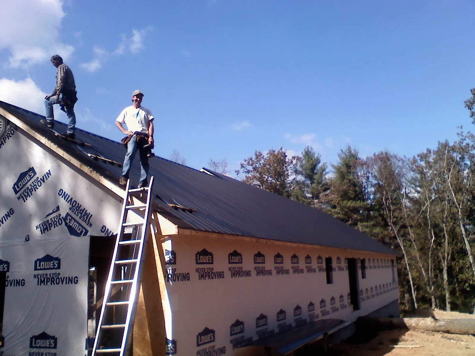 Two roofers standing on a long dark metal roof over a wrapped building in Fair Haven