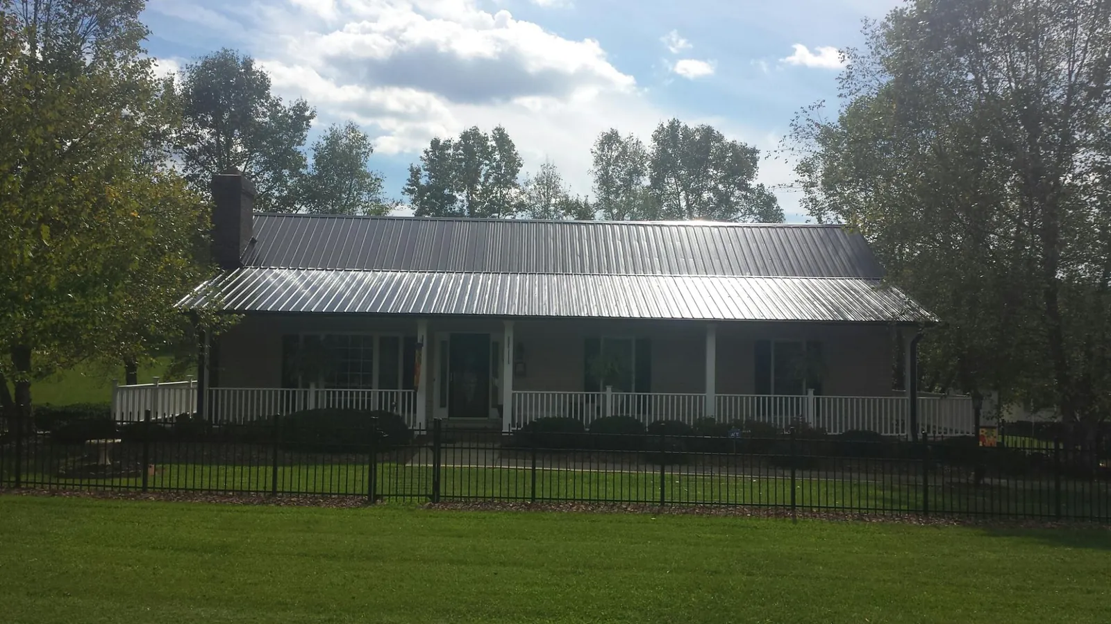 Gray metal roof on a brick ranch with a full width front porch — Gutter Guard Installation work by our crew in Fair Haven